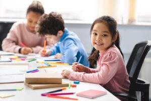 girl drawing at school with two other students